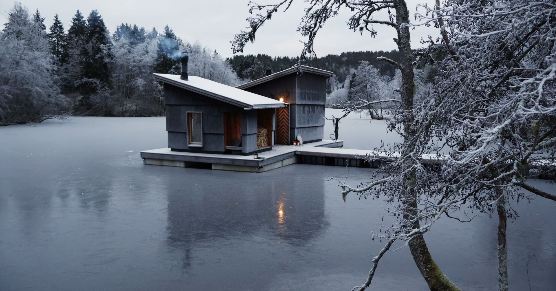 Isolert hytte ved isbelagt innsjø omringet av snødekte trær.