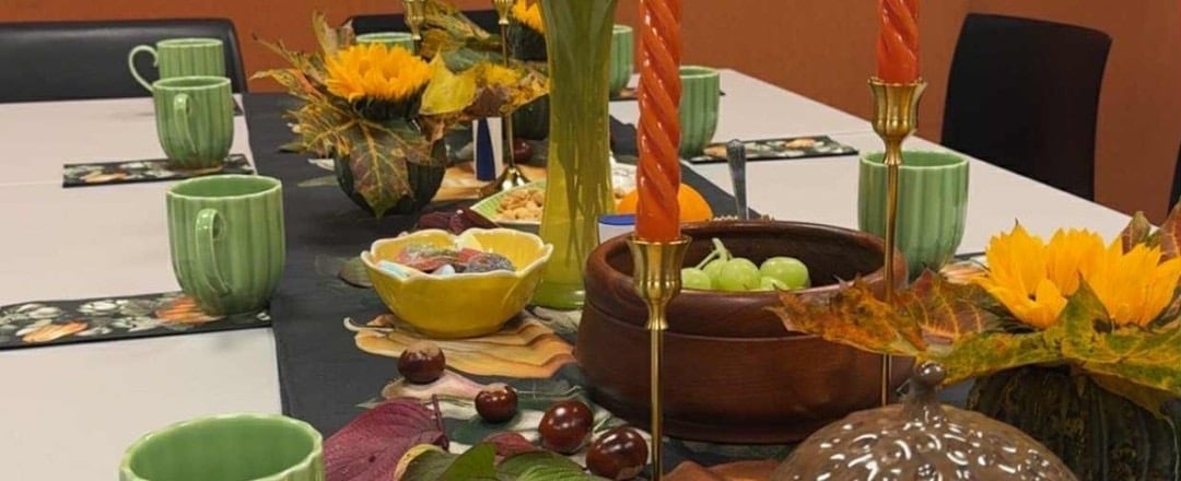 Dekket høstbord med grønne kopper, solblomster, druer, lys og dekorative høstblader.