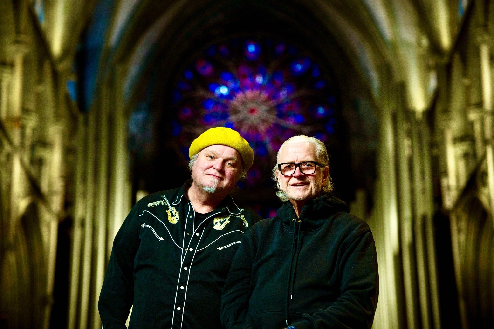 To menn foran en fargerik glassmaleri i en katedral.