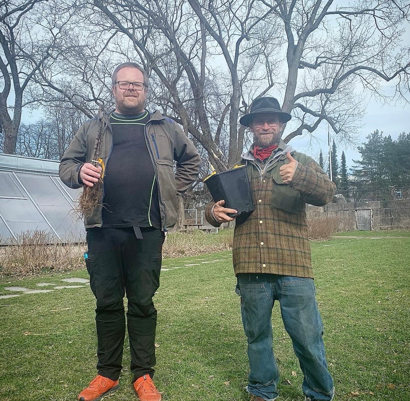 To personer i en hage, en holder en plante, den andre en bøtte, tidlig vår.