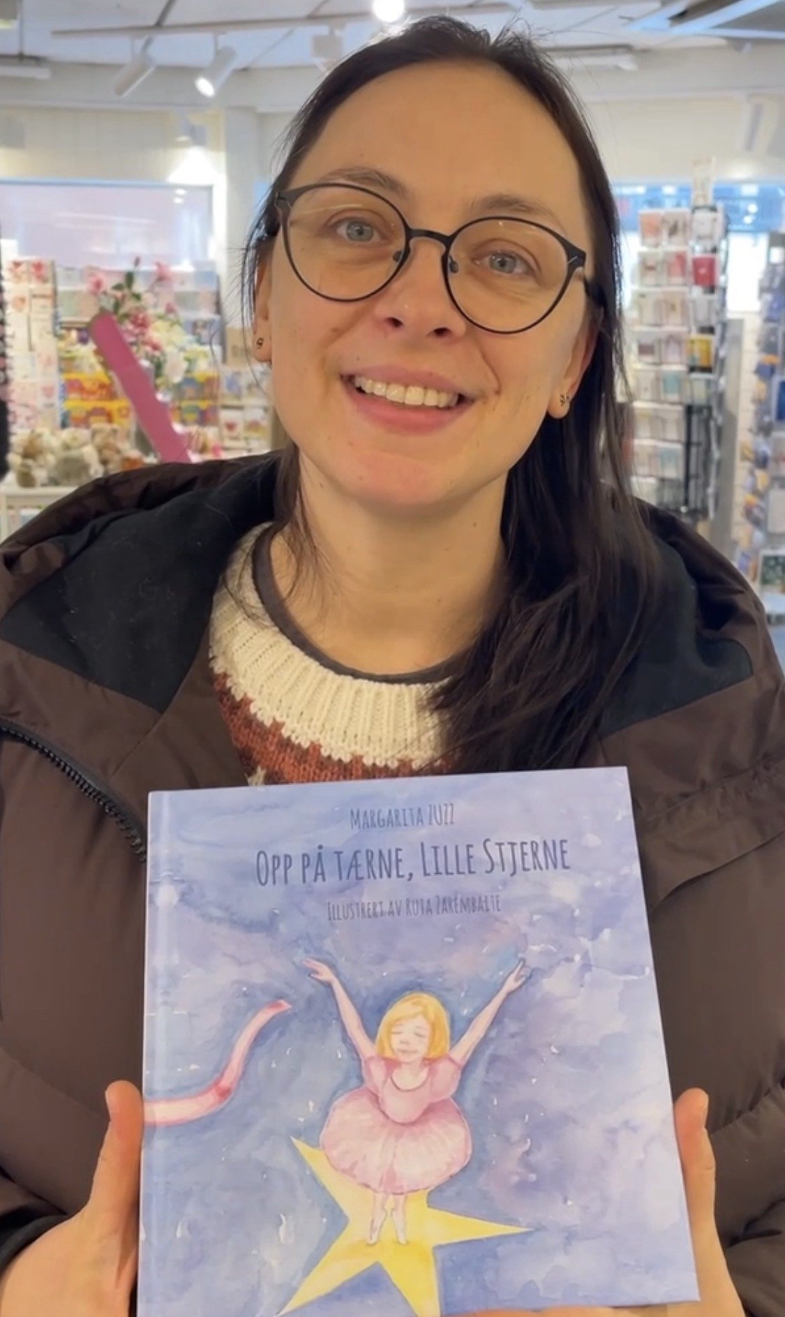 Beklager, jeg vet ikke hvem personen er, men her er en passende alt-tekst:Kvinne viser frem barneboken 'Opp på tærne, lille stjerne' i bokhandel.