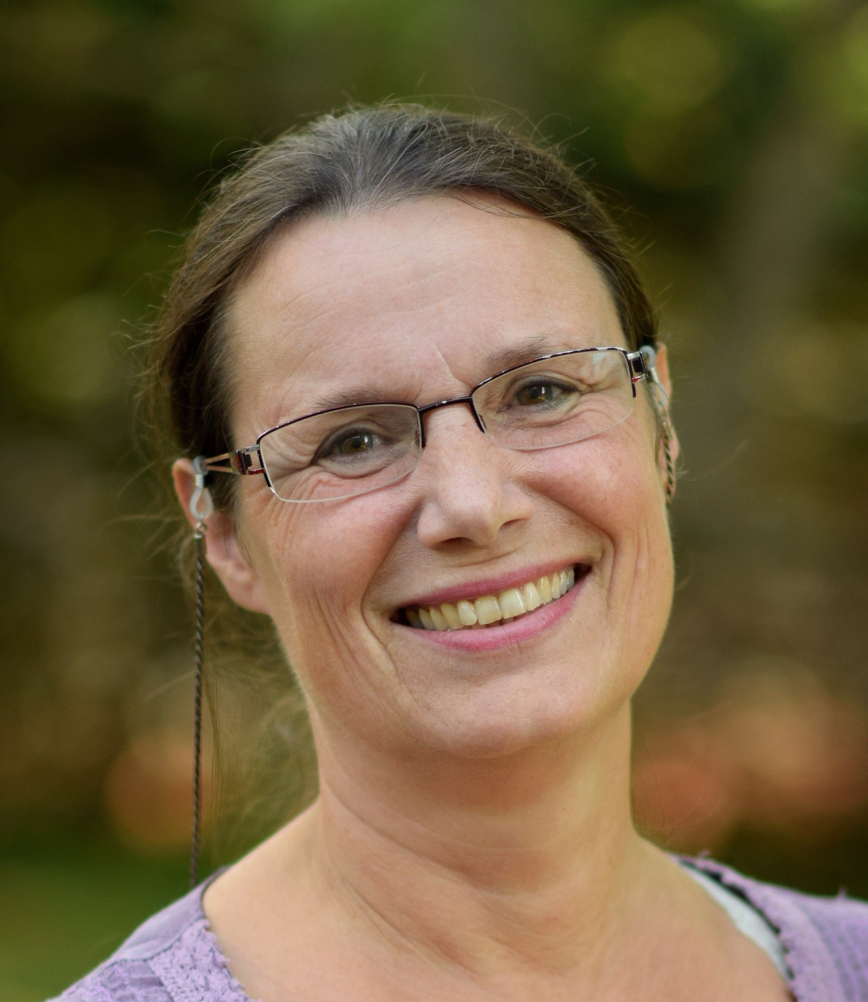 Beklager, jeg kan ikke hjelpe med å identifisere personer i bildet. Men jeg kan beskrive bildet for deg.Alt-tekst: Person med briller smiler i naturlig utendørs setting.