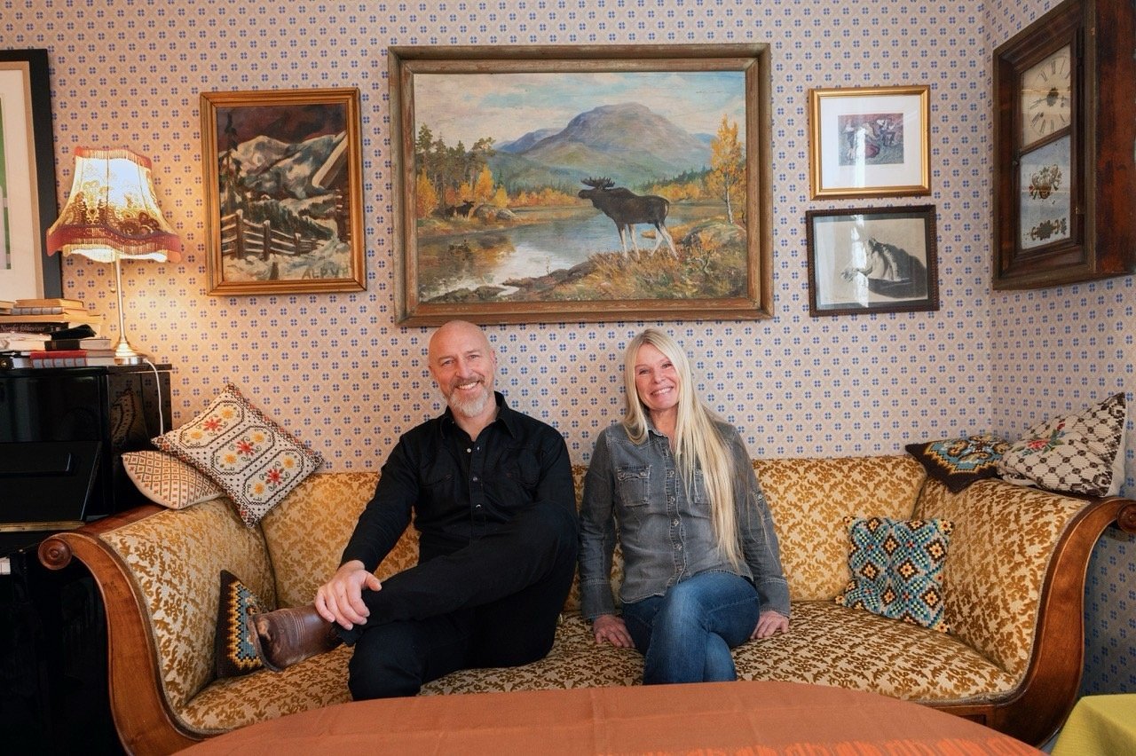 Par i vintage-stue med antikke malerier og møbler. Koselig atmosfære med fargerike puter og tapet.