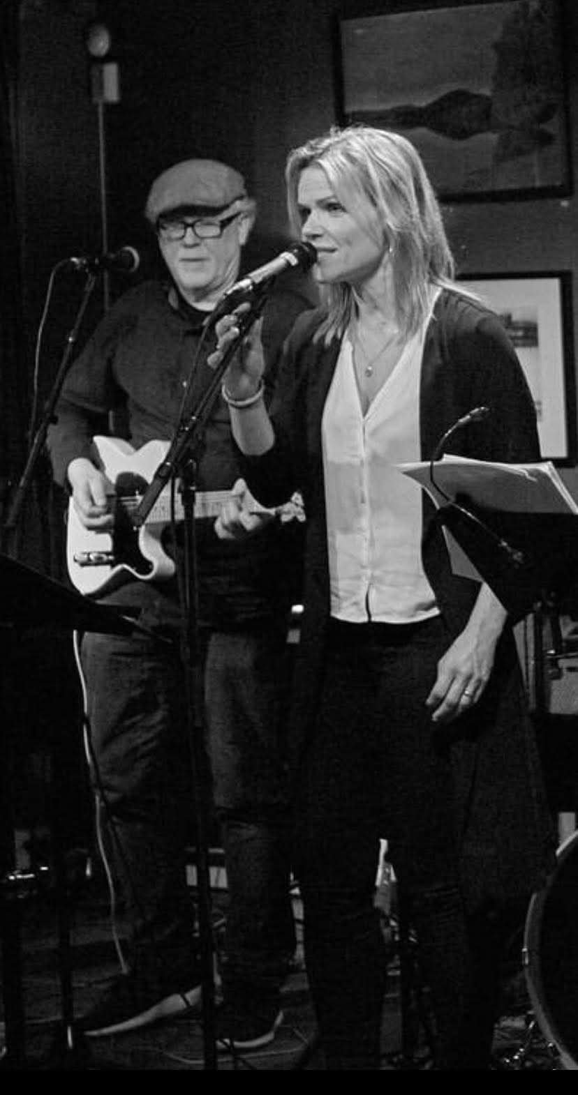 To musikere opptrer på en scene med gitar og mikrofon, svart-hvitt bilde, intim konsertstemning.