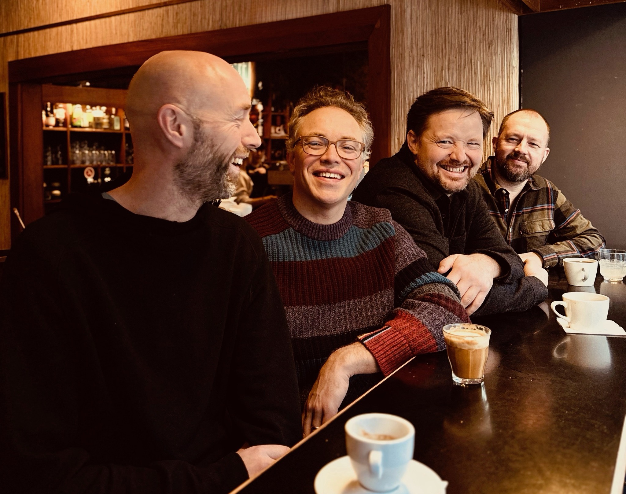 Fire glade menn nyter kaffe sammen i en koselig kafé.