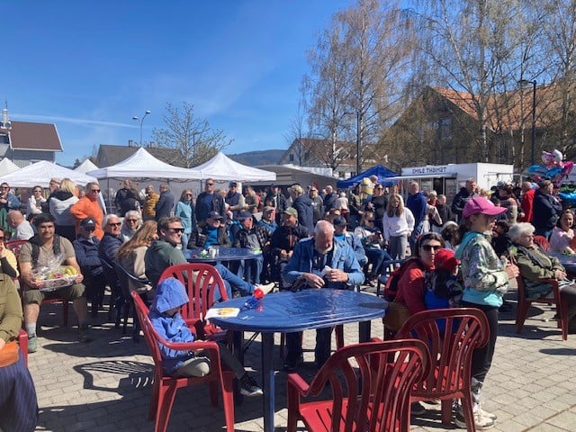 Folkemengde på torget under en solfylt festivaldag, med boder og glade besøkende.