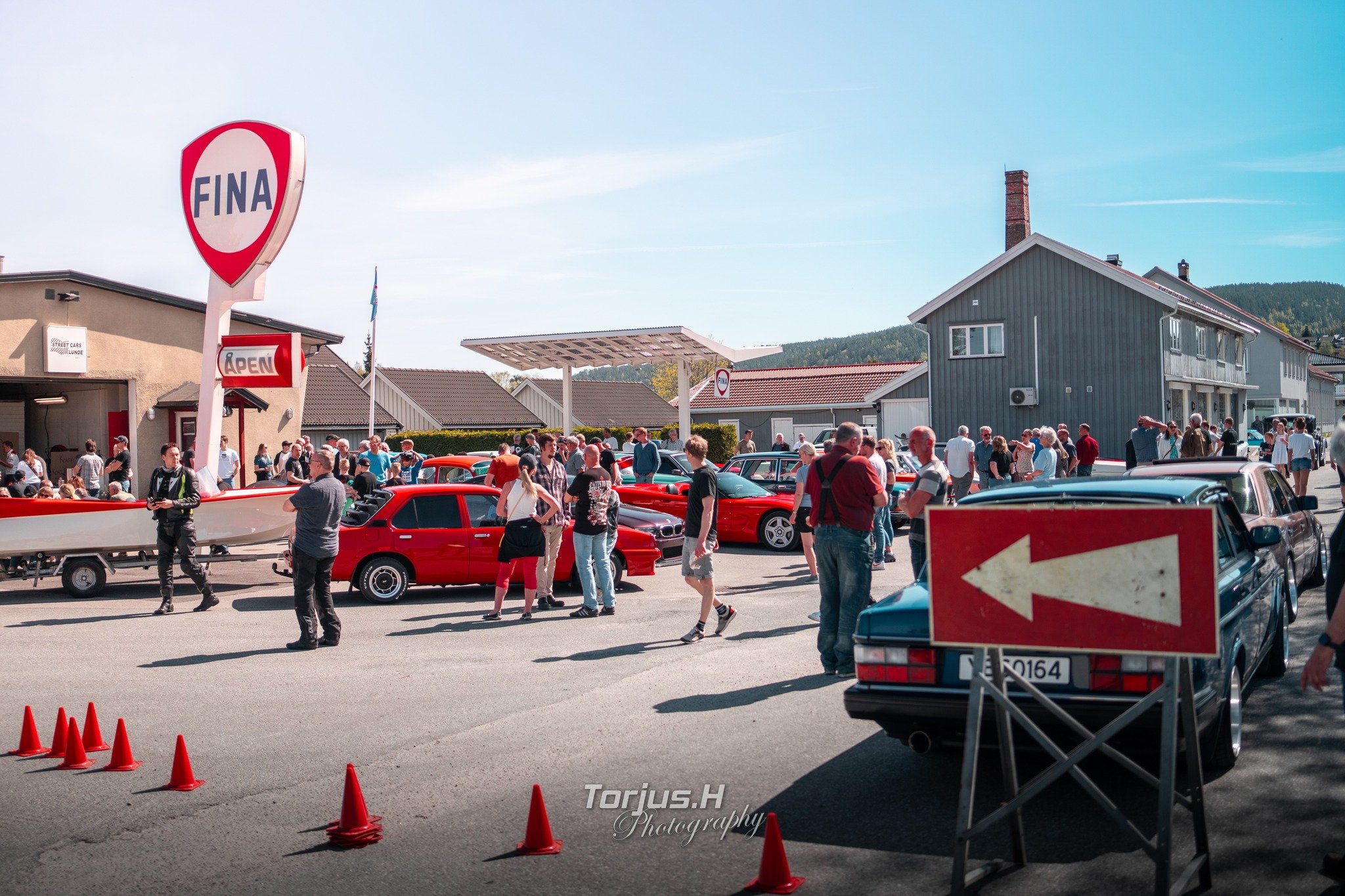 Vårmønstring i Lunde sentrum. Treff med klassiske biler og folkemengde ved FINA-stasjonen i solfylt vær. En livlig dag utendørs.