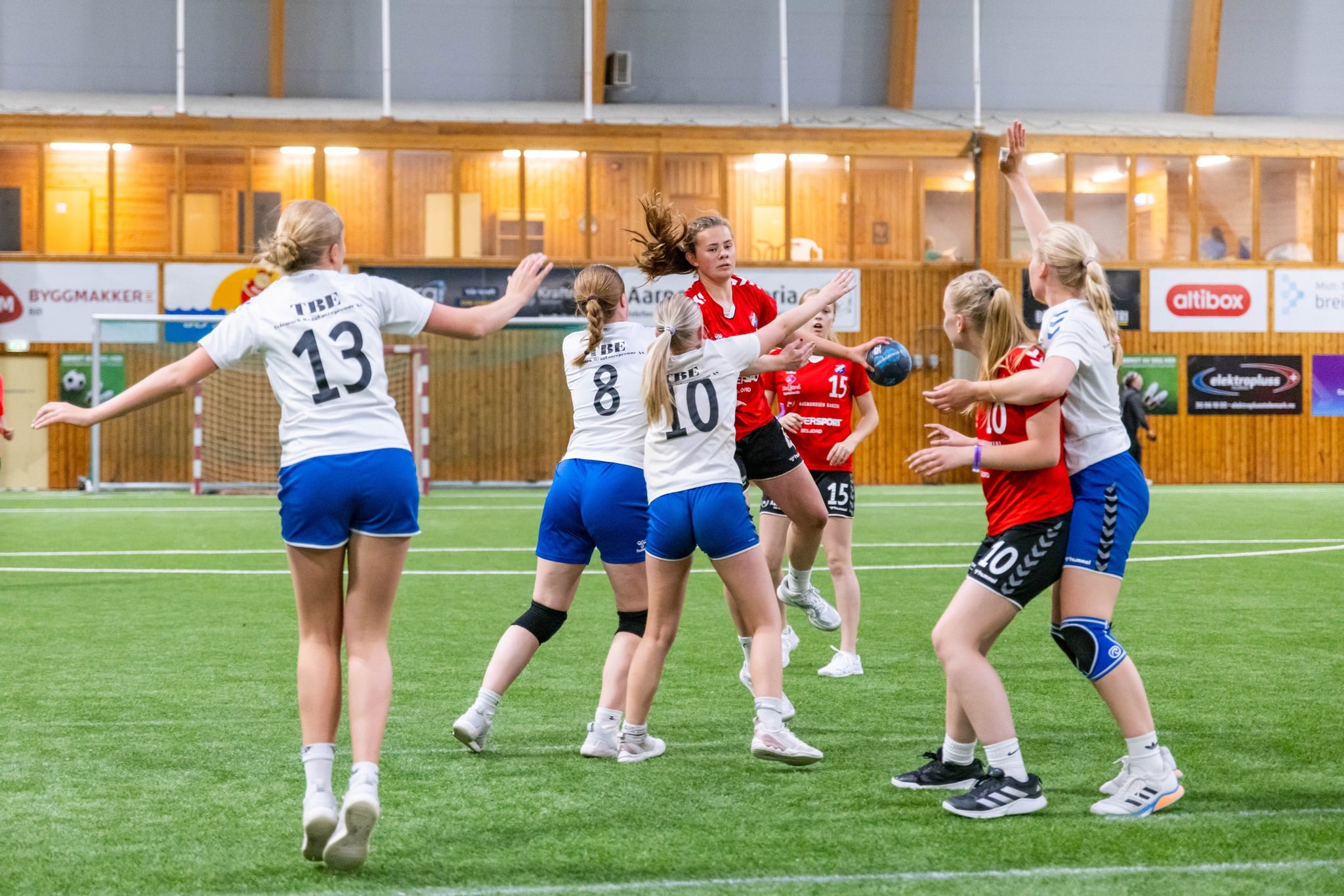 Spillere i håndballkamp i en innendørs arena, med fokus på angrep og samarbeid.