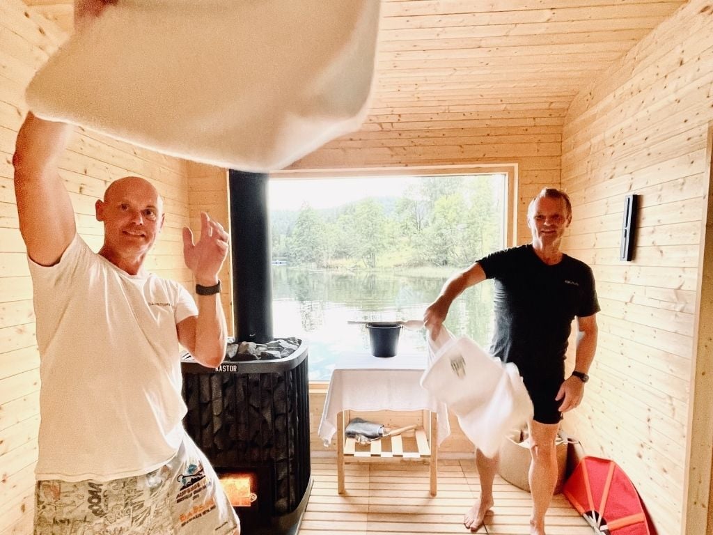 To personer lager atmosfære i en hytte med peis, kaster håndklær mens de nyter utsikten mot vannet.