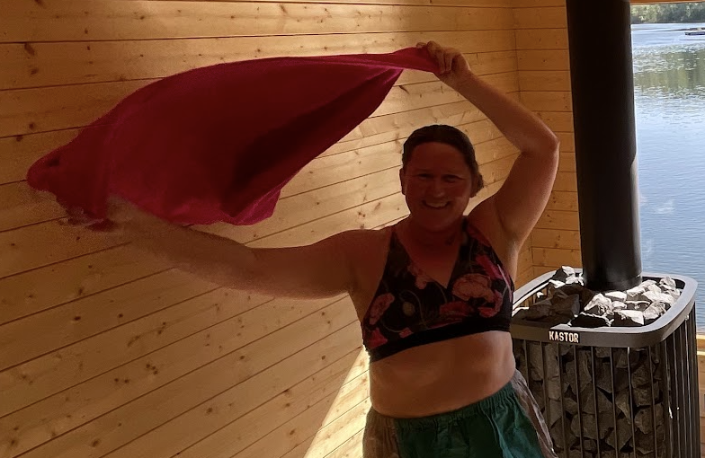 Kvinne som danser med et rødt håndkle i en badstue ved vannet, omfavner sommerens glede.